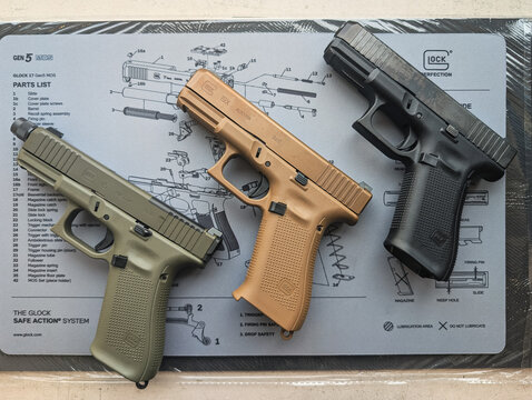 Baltic States, July 11, 2025: New Austrian Glock pistols in a gun shop: models 19X (Coyote), 45 (Olive Green), and 19 Gen5 (Black), displayed on a branded cleaning mat with a diagram.