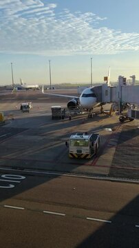 Airplane parked at airport terminal gate with jet bridge connected. Ground crew and support vehicles on the tarmac preparing for departure or arrival. Air travel and transportation concept. Vertical.