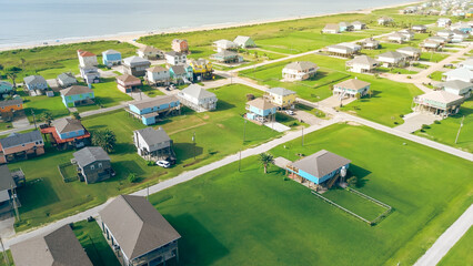 Long stretch of oceanfront residential development with low-density colorful raised beach houses, set apart by spacious grassy backyards, vacant land near sandy shoreline in Port Bolivar, Texas