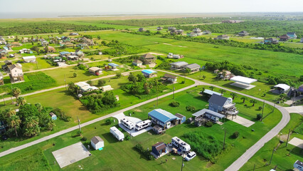 RVs and trailers parked across lots near Beach Boyt in Port Bolivar, Texas, mix of permanent residents and vacationers. Community arranged in open layout with maintained lawns, gravel paved road
