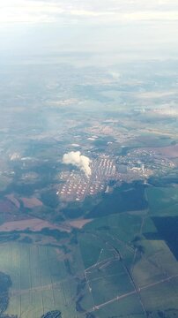 Aerial view of a large industrial plant with numerous storage tanks and a plume of smoke, situated between a sprawling city and vast green agricultural fields, illustrating industrial impact. 4k.
