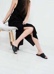 Beautiful young woman in a black dress and summer opened shoes are sitting on the chair