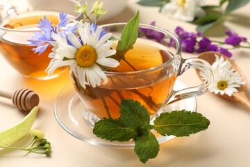 Aromatic herbal tea in glass cups, different flowers and mint on beige background, closeup