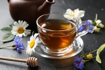 Aromatic herbal tea in glass cup, different flowers and teapot on black table, closeup