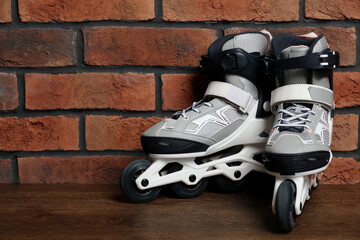Pair of roller skates on wooden table near brick wall, space for text