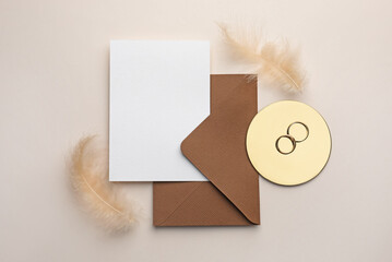 Wedding invitation card, envelope, gold rings and feather on beige background, flat lay