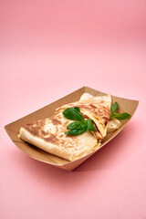Delicious grilled quesadilla with basil on kraft paper tray against pink background
