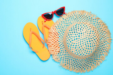 Straw hat, flip flops and sunglasses on light blue background, flat lay