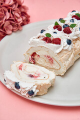 Delicate meringue roulade with whipped cream berry topping and hydrangea arrangement on pink