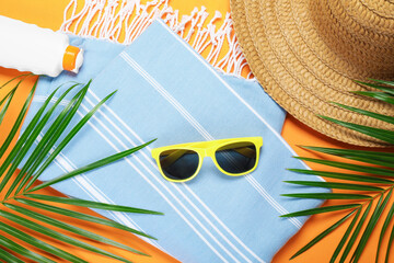 Beach accessories and palm leaves on orange background, flat lay