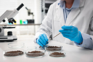 Scientist taking soil sample for research at white table in laboratory, closeup