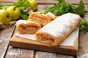 Tasty apple strudels with powdered sugar, mint and fruits on wooden table, closeup