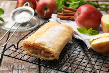 Tasty apple strudel with powdered sugar, mint, fruits and cinnamon on wooden table, closeup