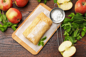 Tasty apple strudel with powdered sugar, mint and fruits on wooden table, flat lay