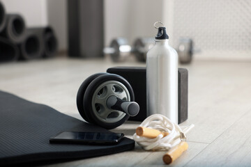Phone and different fitness equipment on floor in gym, closeup