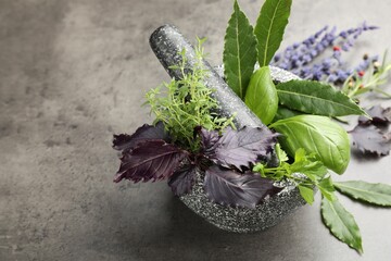 Mortar with pestle, different aromatic herbs and spices on grey table, closeup. Space for text
