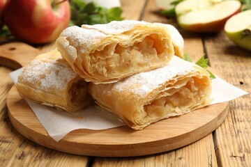 Pieces of tasty apple strudel with powdered sugar on wooden table, closeup