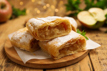 Pieces of tasty apple strudel with powdered sugar on wooden table, closeup