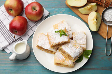 Pieces of tasty apple strudel with powdered sugar, mint and fruits on light blue wooden table, flat...