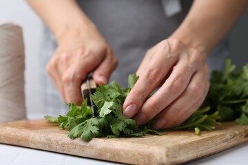 Woman cutting fresh cilantro at white table, closeup