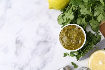 Tasty sauce with cilantro and lemons on white marble table, flat lay. Space for text