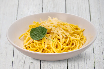 Tagliolini spaghetti egg pasta with butter and sage sauce with parmesan flakes in white dish on...
