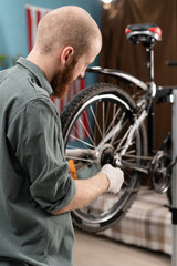 Bearded cyclist fixing bicycle wheel with wrench repairing and servicing bicycle at home DIY.