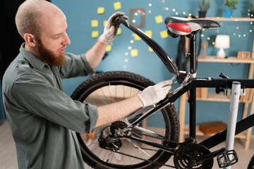 Young bearded man performing maintenance and repair on mountain bike at home. Concept of servicing...