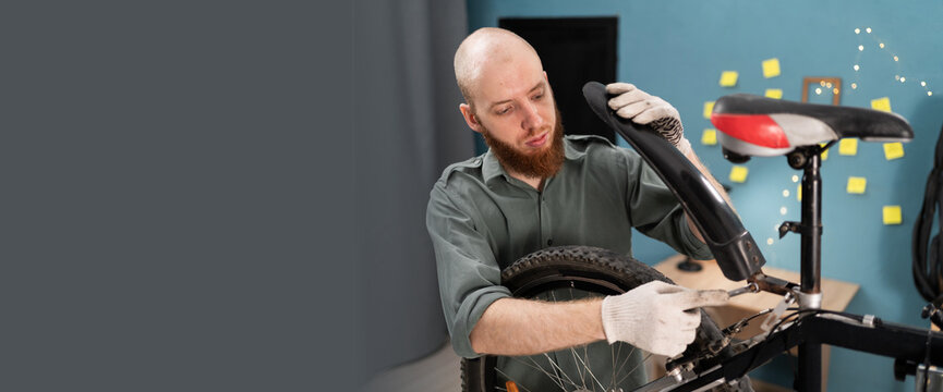 Young bearded man performing maintenance and repair on mountain bike at home. Concept of servicing bicycle