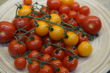 Cherry tomatoes yellow and red on branches on a bamboo plate