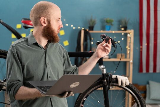 Bearded man doing bike servicing searching replacement components on laptop working at home. repairing bicycle