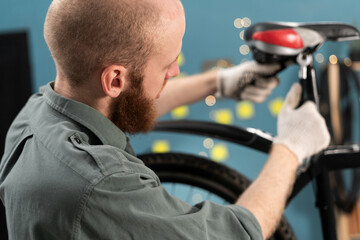 bearded man using wrench in process of repairing and servicing bicycle at home.