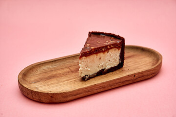 Decadent cheesecake slice on rustic wooden tray against pink backdrop