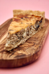 Delicious homemade mushroom and cheese quiche on wooden plate with pink background