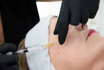 Beautician injecting hyaluronic acid into woman's face for facial rejuvenation treatment