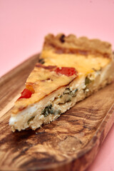 Delicious quiche slice with tomatoes and spinach on wooden board