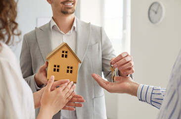 Cropped shot of unknown man broker holding model of house and giving keys to new apartment for...