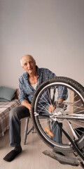 Portrait of senior repairing bicycle at home looking at camera. Hobby and leisure concept