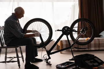 Silhouette of a retired man repairing and checking his bicycle at home. Bicycle repair and...