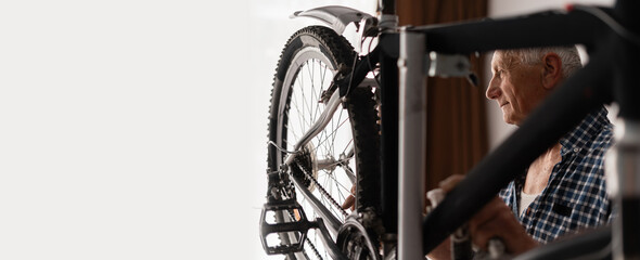 Old man rear wheel adjustment. Elderly repairman working at home repairing his bicycle. Banner.