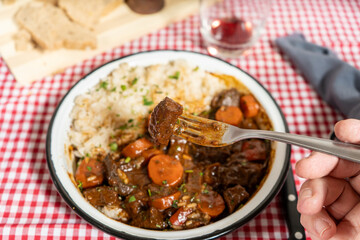 Fork holding piece of meat over bowl of beef stew with rice