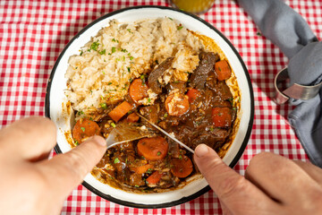 Hands cutting into hearty beef stew with rice