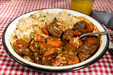 Hearty beef stew with carrots and rice on checkered tablecloth
