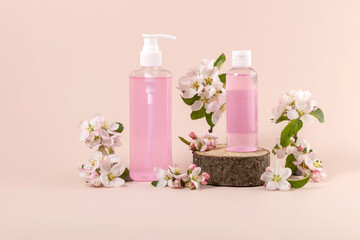 cosmetics containers on a wooden podium and branches of a blooming apple tree on a beige background