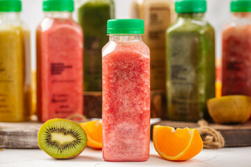 Red smoothie in plastic bottle with kiwi and orange on white table