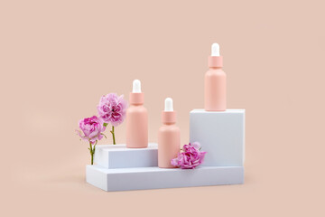 a set of bottles with an essential oil pipette on a white podium and purple rose flowers on a beige background