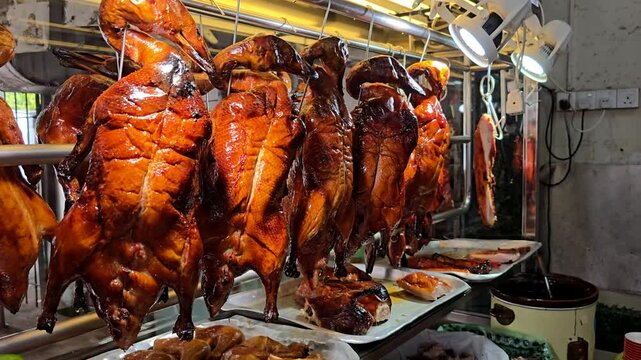 Roast ducks hanging under lights at a Chinese hawker stall, freshly cooked and ready for serving.