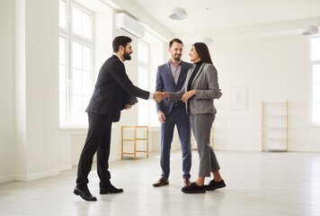 Happy smiling young couple customers shaking hands with professional man realtor making deal buying...