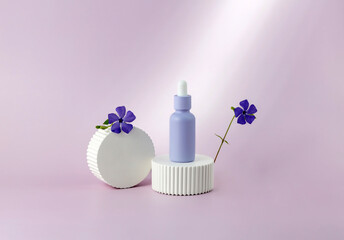 bottle of essential oil with a pipette and periwinkle flowers on a white podium on a purple...