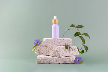 a bottle with an essential oil pipette on a stone podium and periwinkle flowers and twigs